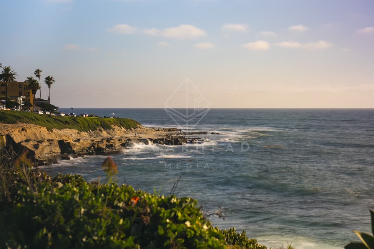 Elevated view of the cliffs, the surf and palm trees at La Jolla Cove, with people walking.