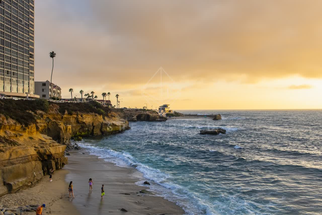 Elevated view of the cliffs, the surf and palm trees at La Jolla Cove, with people walking.