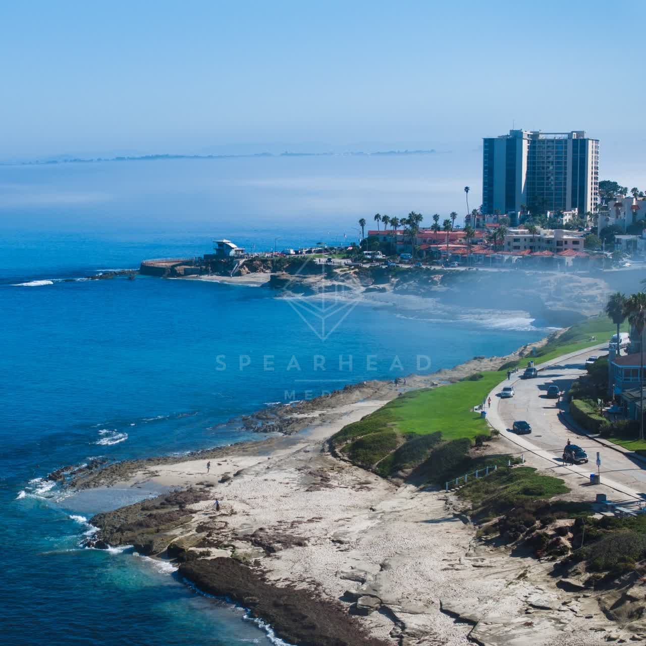 Aerial view of the cliffs, palm trees and the ocean at Windansea, with people walking.