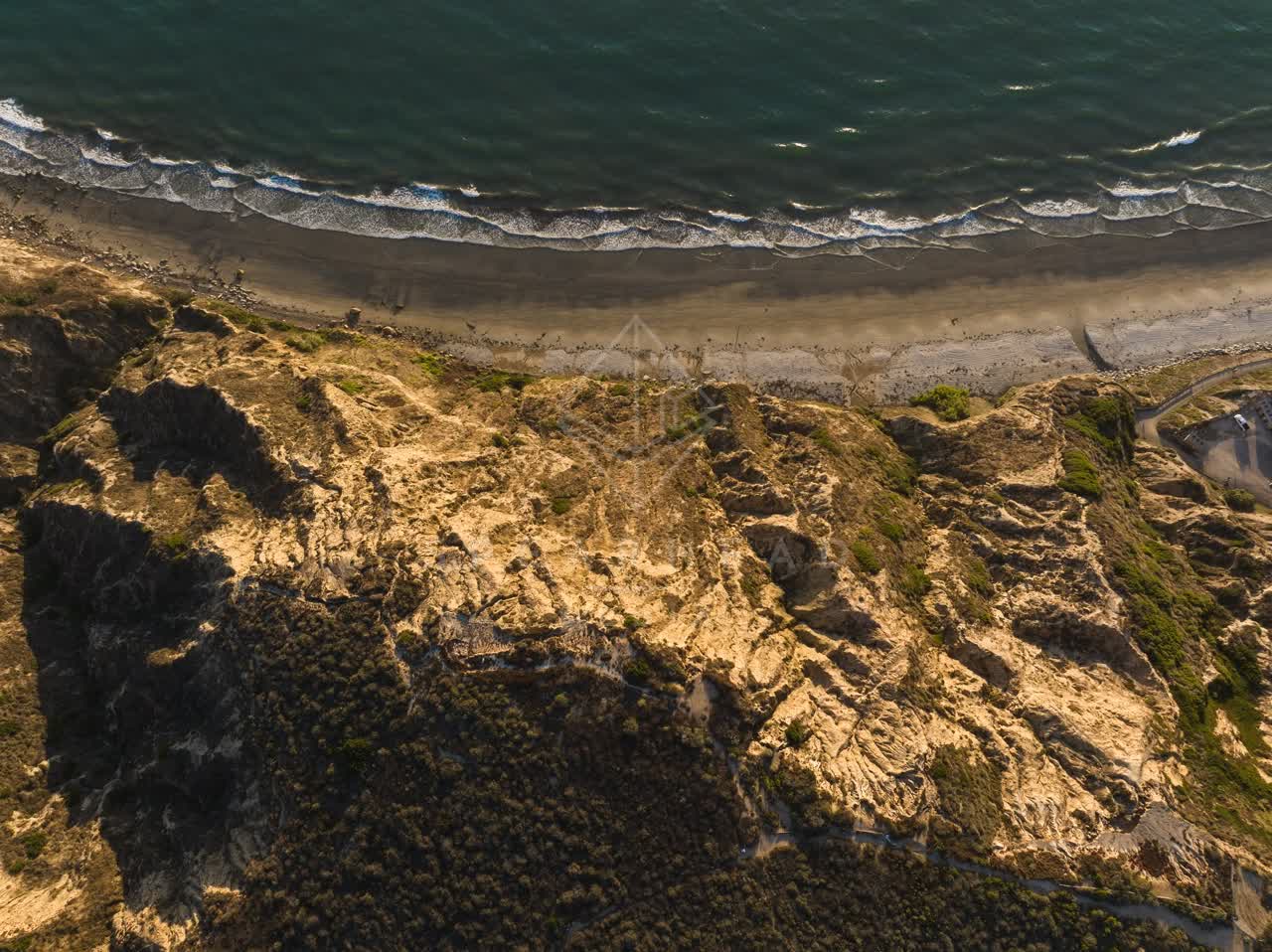 Aerial view of the cliffs, the surf and the ocean at Black’s Beach, with people walking.