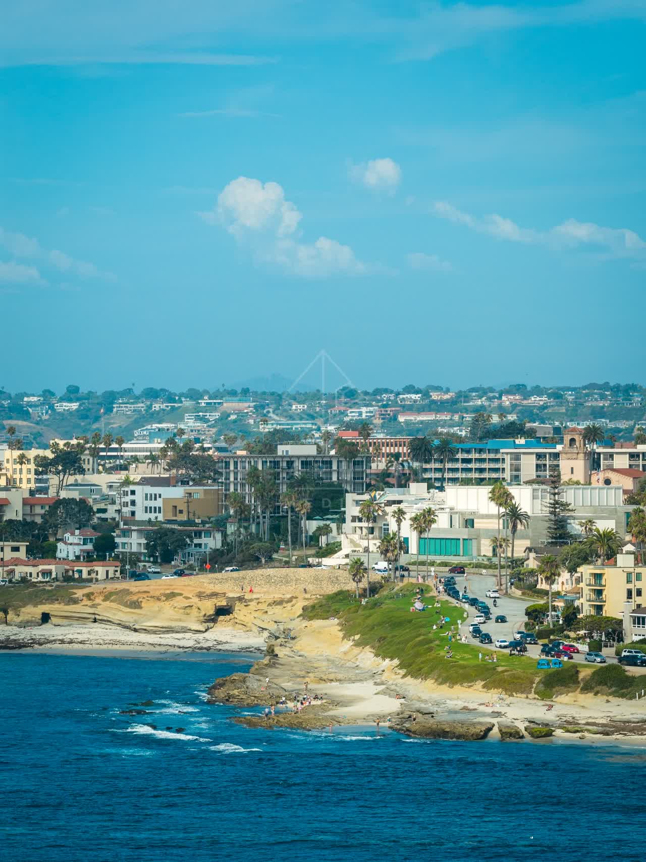 Aerial view of the cliffs, palm trees and the ocean at La Jolla Cove, with people walking.