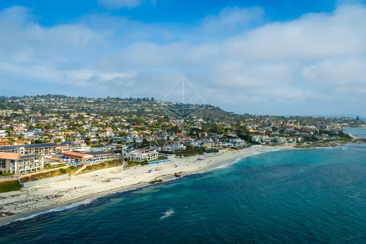 Aerial view of the beach, the ocean and homes in La Jolla, with people walking.