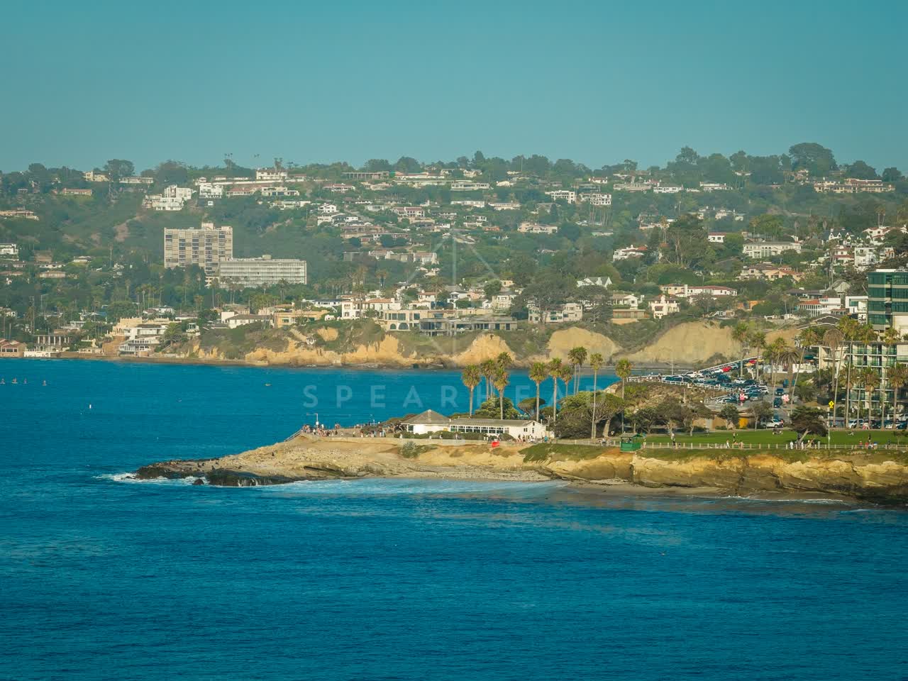 Aerial view of the cliffs, palm trees and the ocean at La Jolla Cove, with people walking.