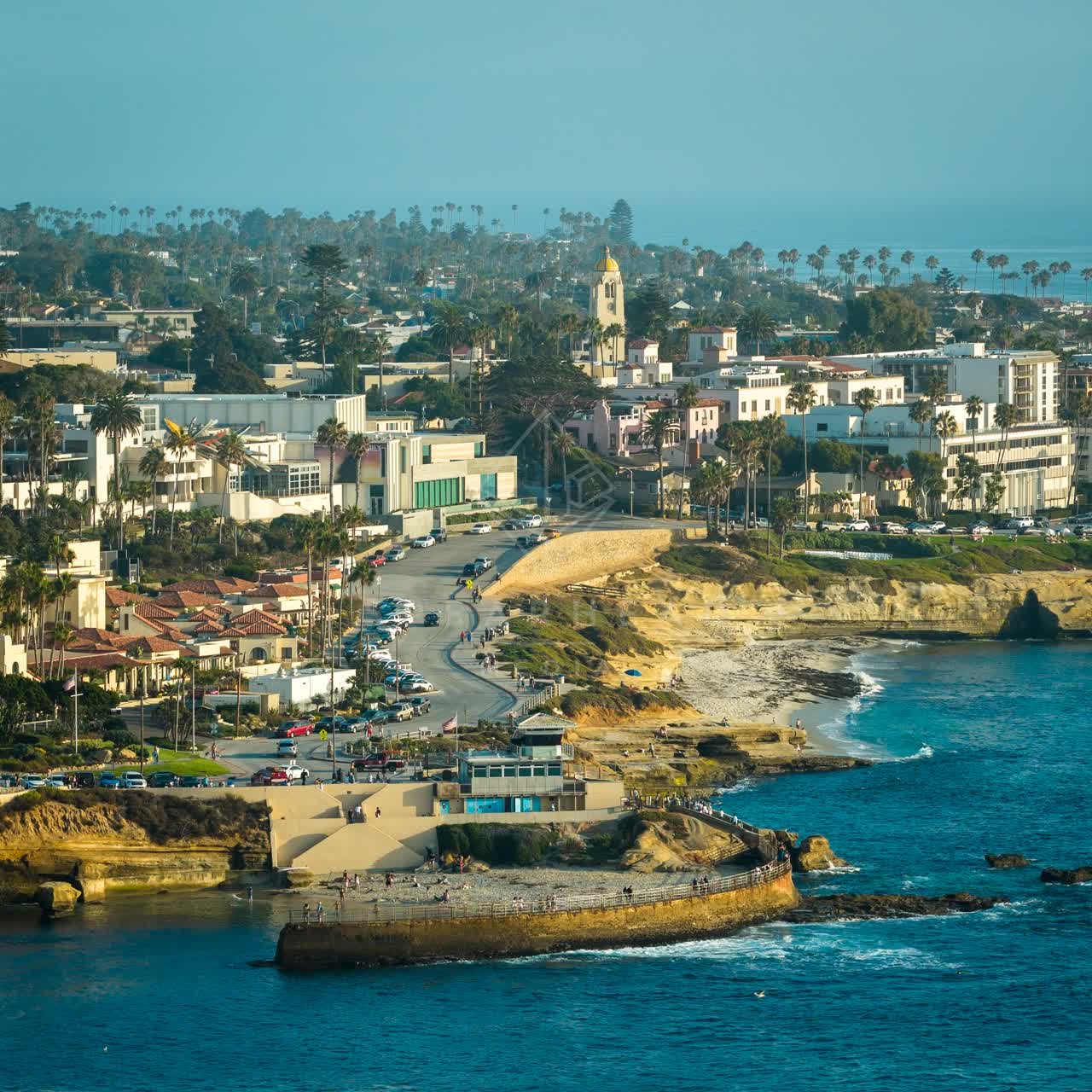 Aerial view of the cliffs, palm trees and the ocean at Village of La Jolla, with people walking.