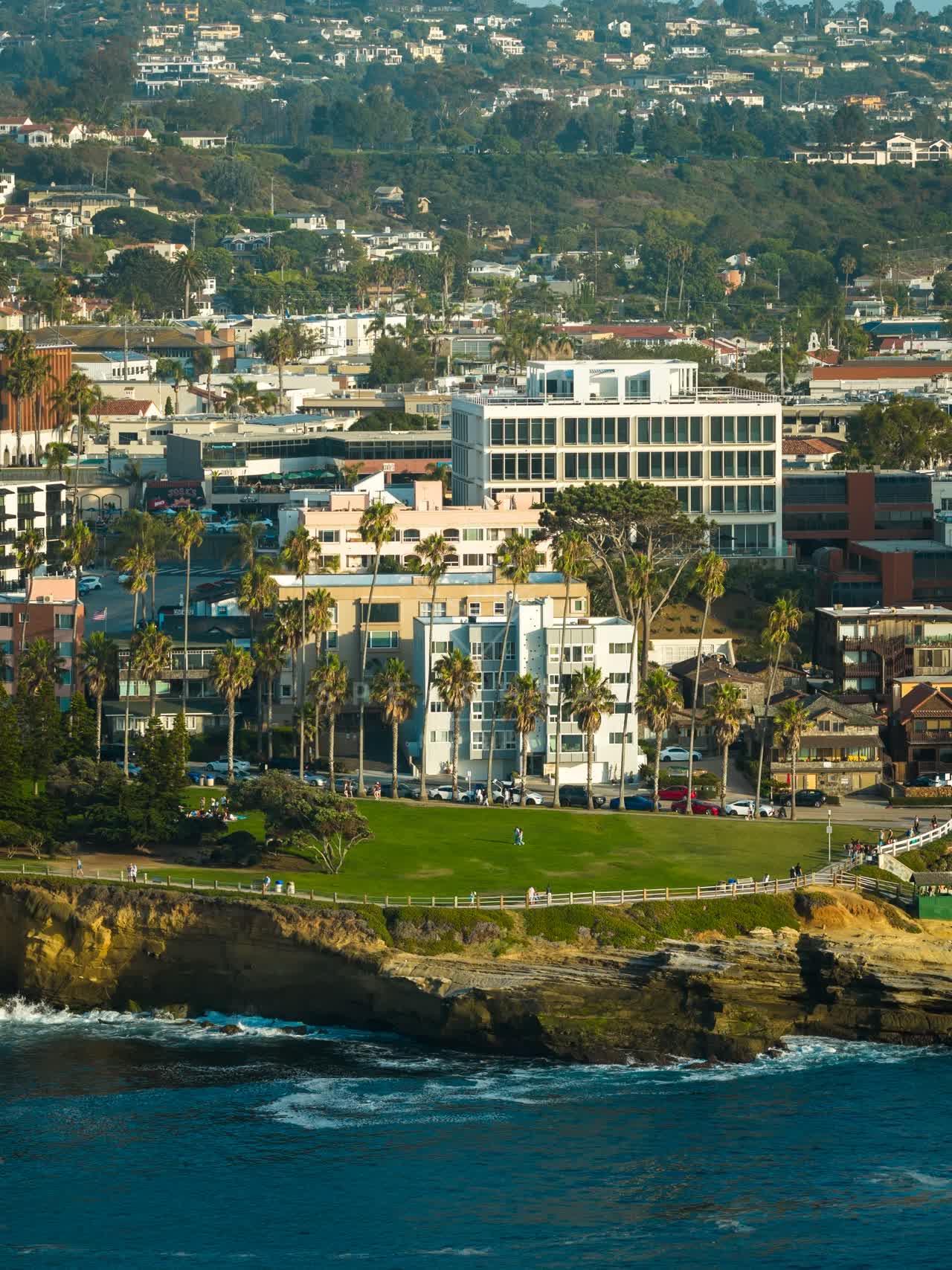Aerial view of the cliffs, palm trees and the ocean at La Jolla Cove, with people walking.