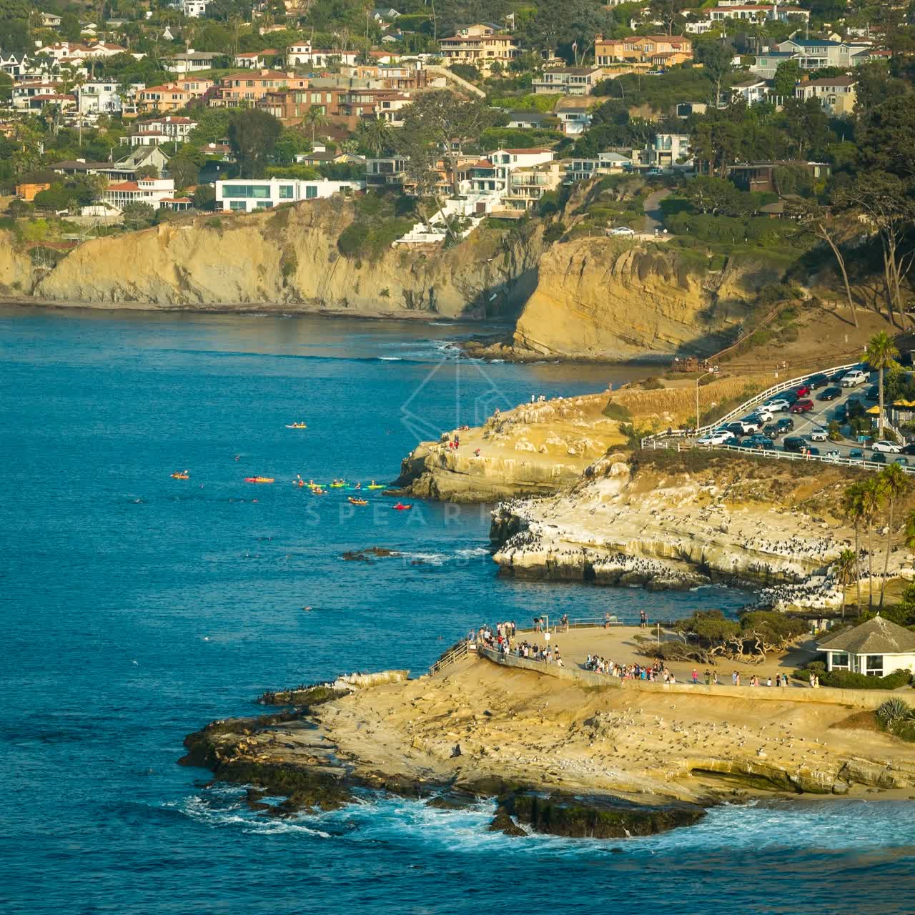 Aerial view of the cliffs, boats and wildlife at La Jolla Cove, with a crowd gathered.