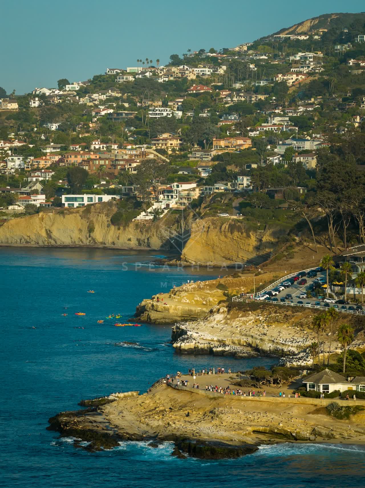 Aerial view of the cliffs, boats and palm trees at La Jolla Cove, with paddlers on the water.
