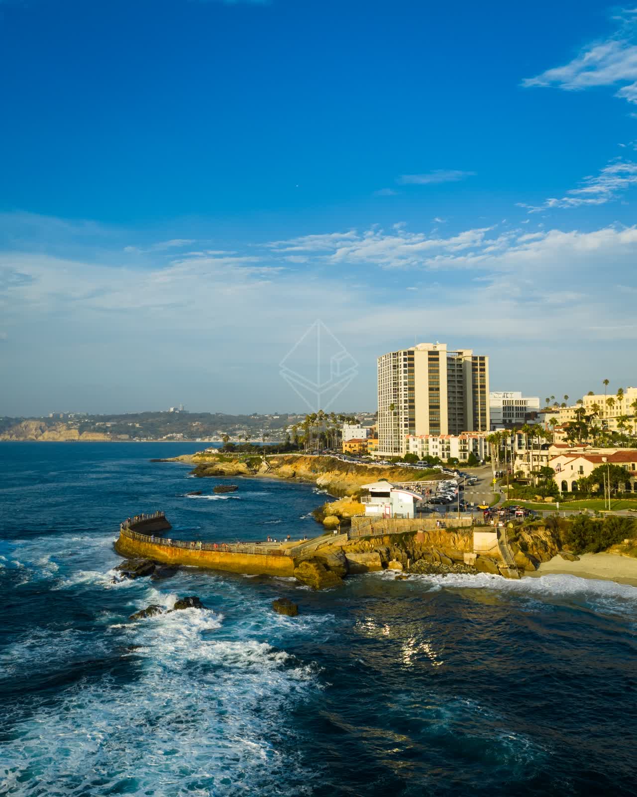 Aerial view of the cliffs, the surf and palm trees at Village of La Jolla, with people walking.