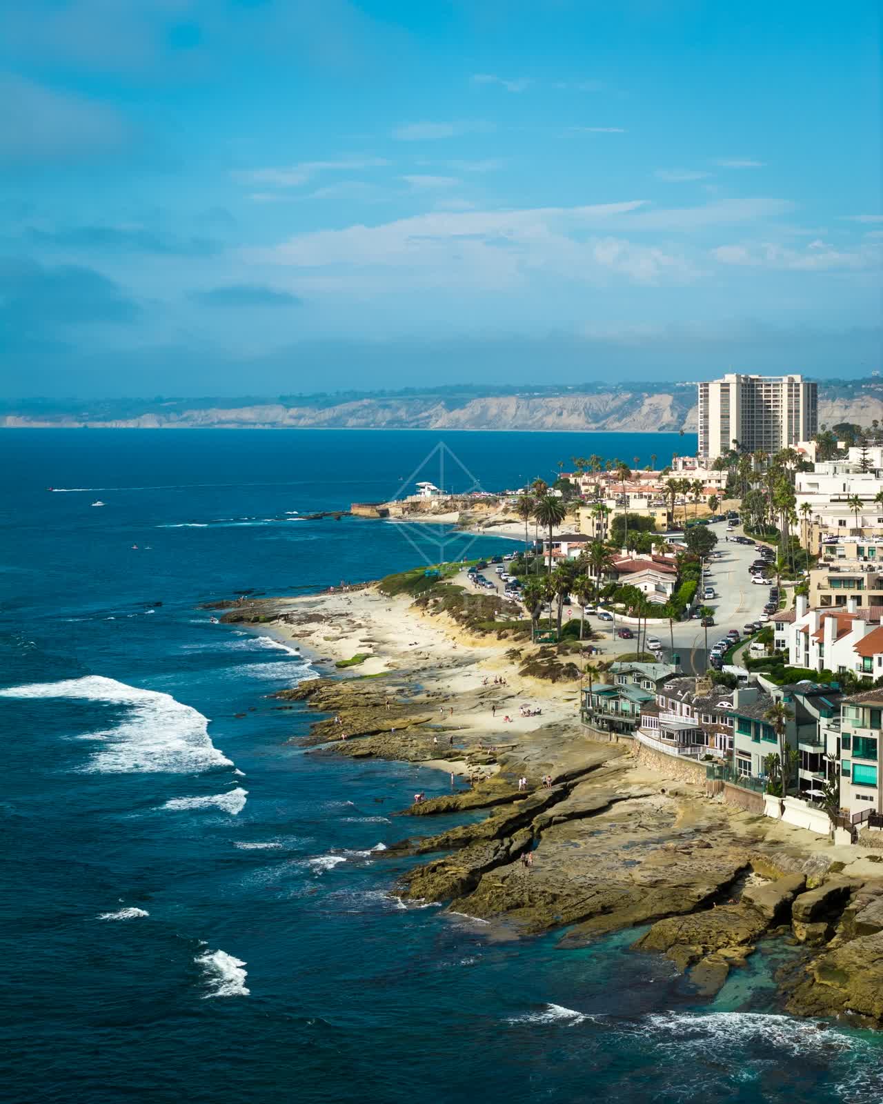 Aerial view of the cliffs, the surf and palm trees at Village of La Jolla, with people walking.