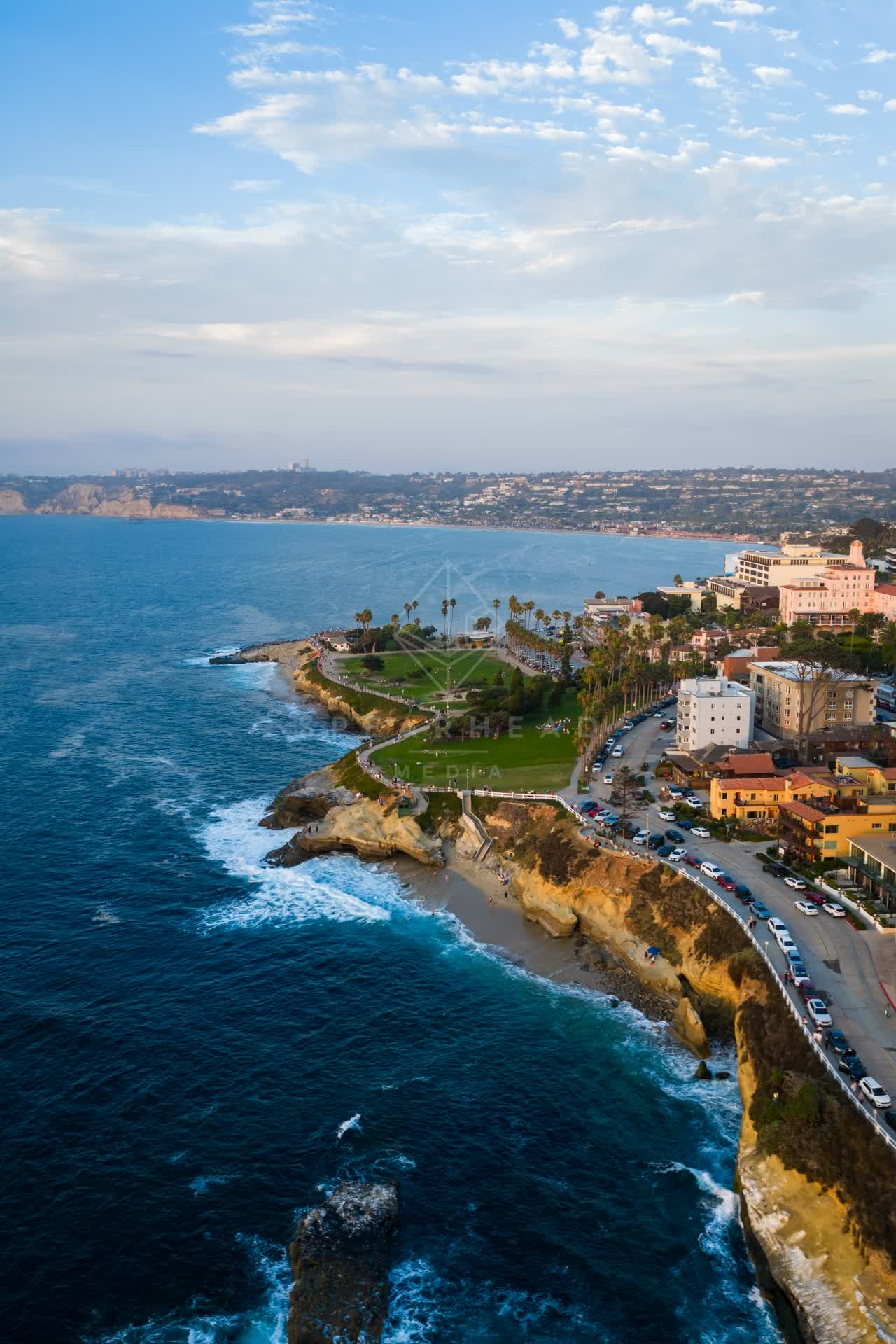 Aerial view of the cliffs, palm trees and the ocean at Village of La Jolla, with people walking.