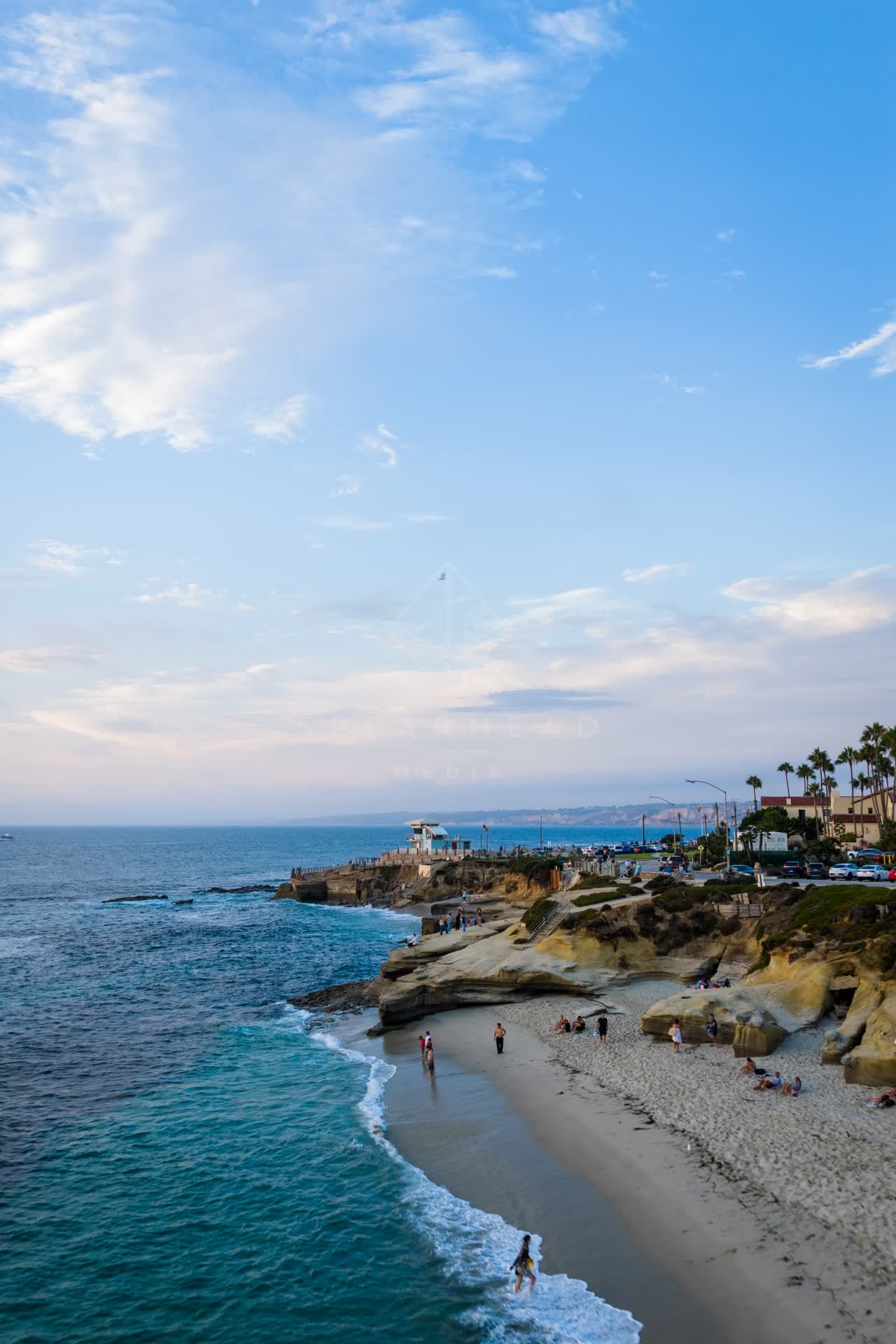 Aerial view of the cliffs, palm trees and the ocean at Village of La Jolla, with people walking.