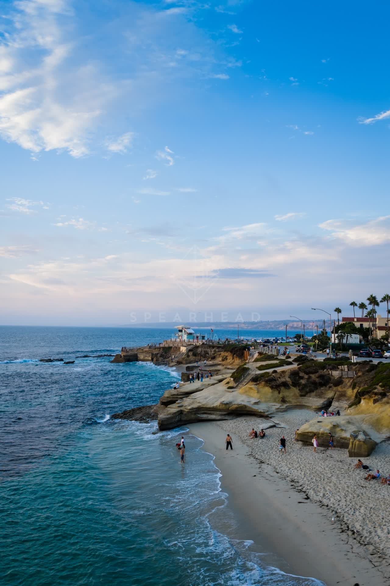 Low aerial view of the beach, palm trees and the ocean at Village of La Jolla, with people walking.