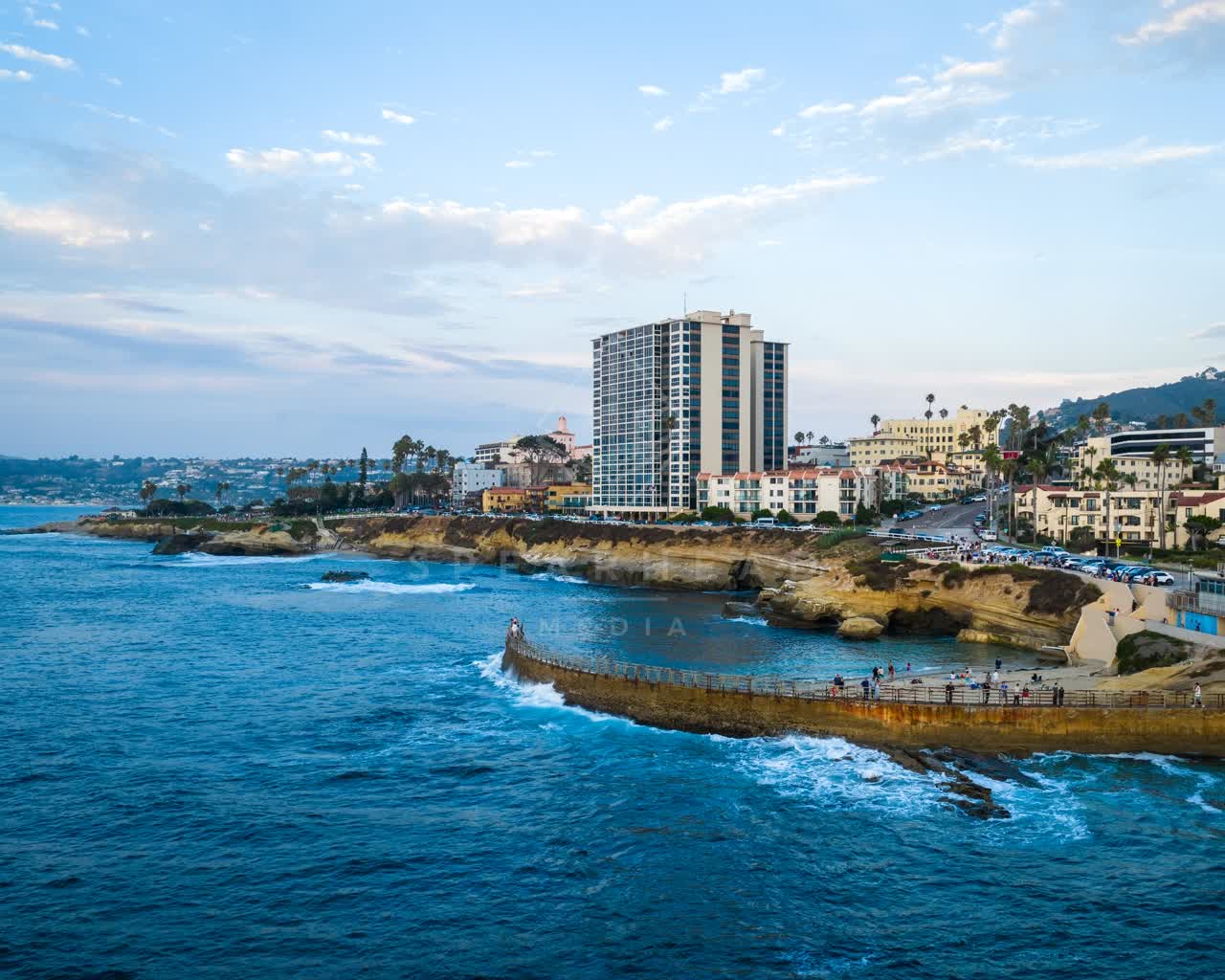 Aerial view of the cliffs, the surf and the ocean at Village of La Jolla, with people walking.