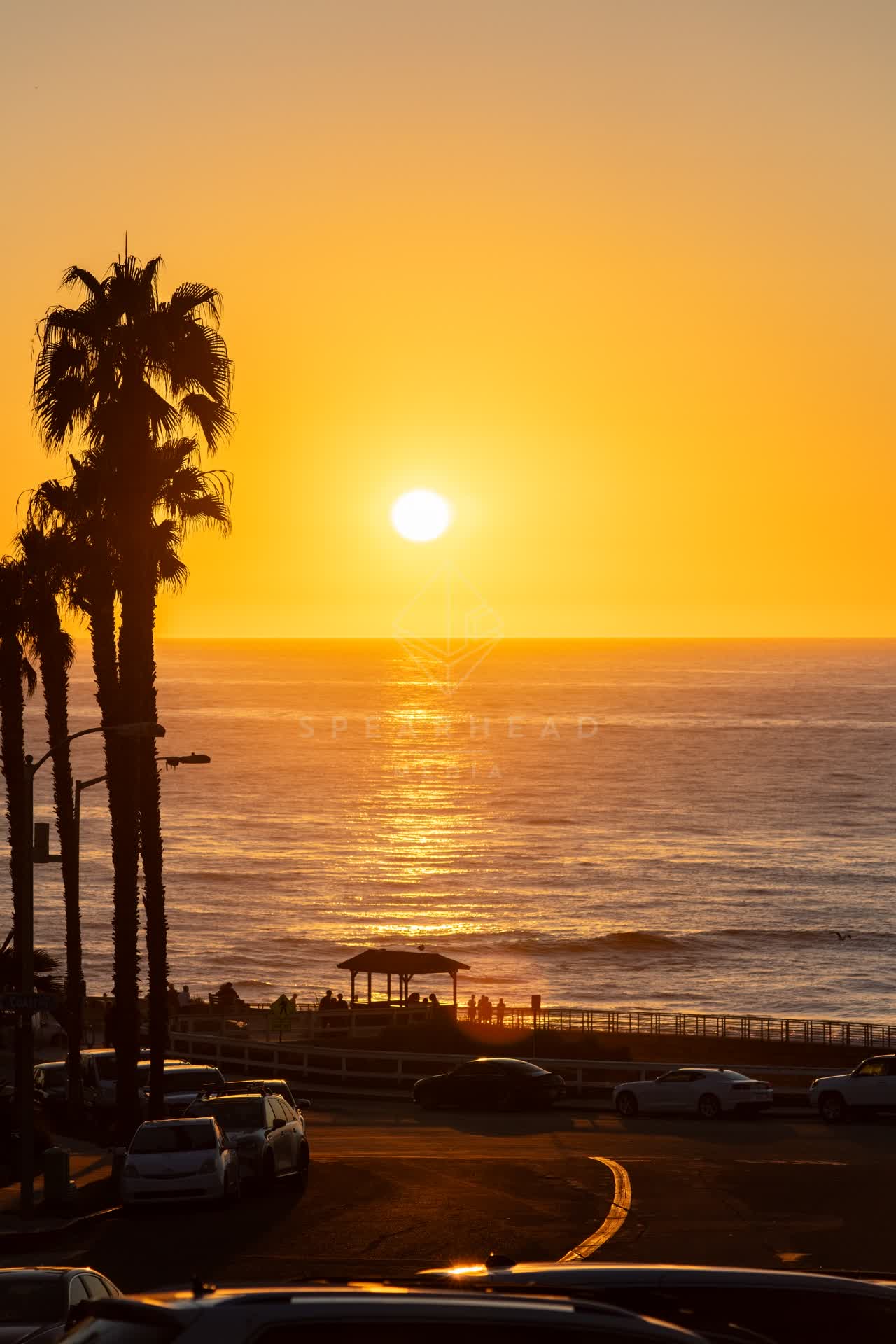Elevated view of the beach, palm trees and the ocean at La Jolla Cove, with people walking.