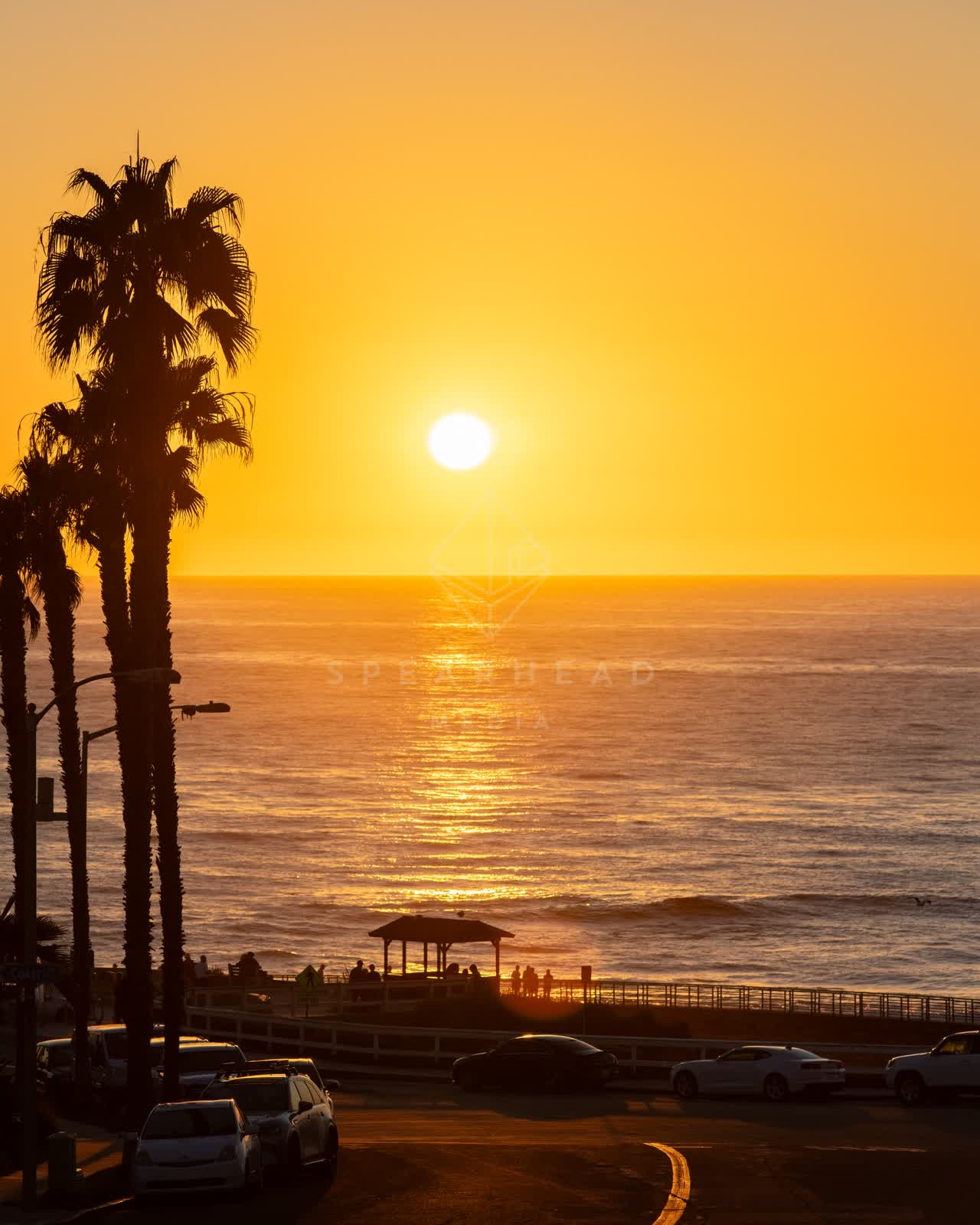 Elevated view of the beach, palm trees and the ocean at La Jolla Cove, with people walking.