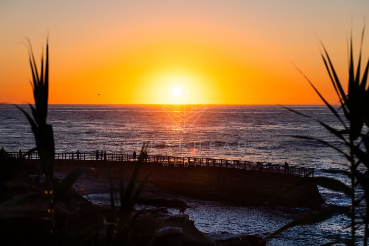Elevated view of the cliffs, the pier and the ocean at La Jolla Cove, with people walking.