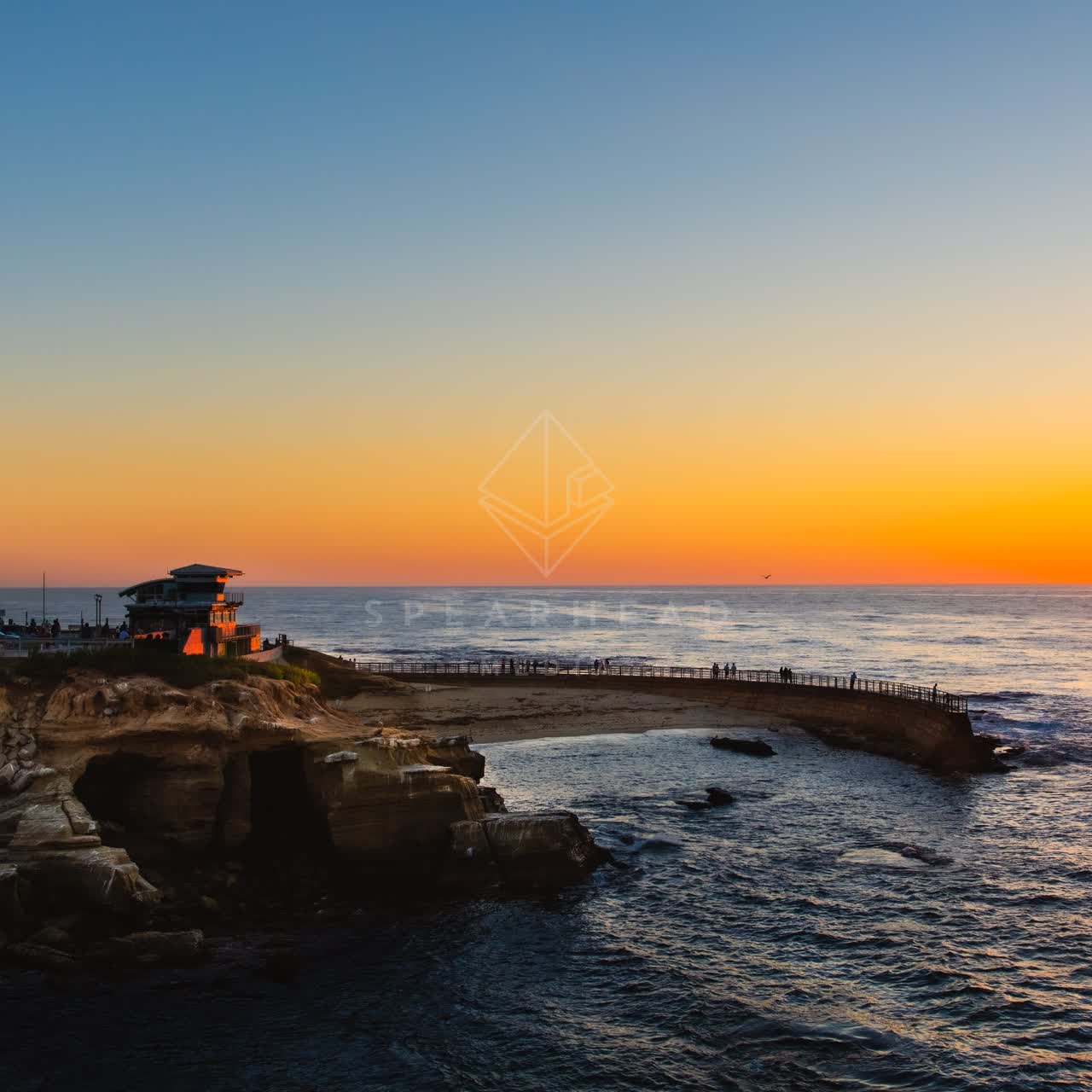 Low aerial view of the cliffs, the pier and the ocean at La Jolla Cove, with people walking.