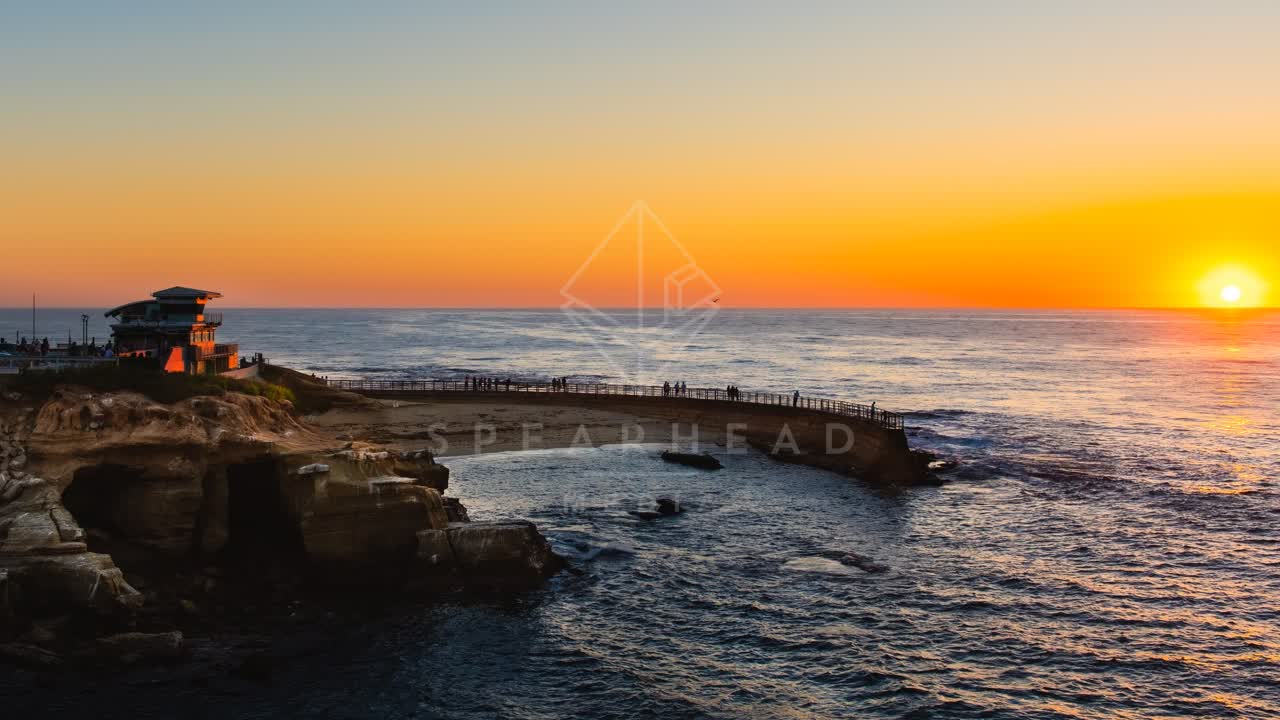 Low aerial view of the cliffs, the ocean and the beach at La Jolla Cove, with people walking.