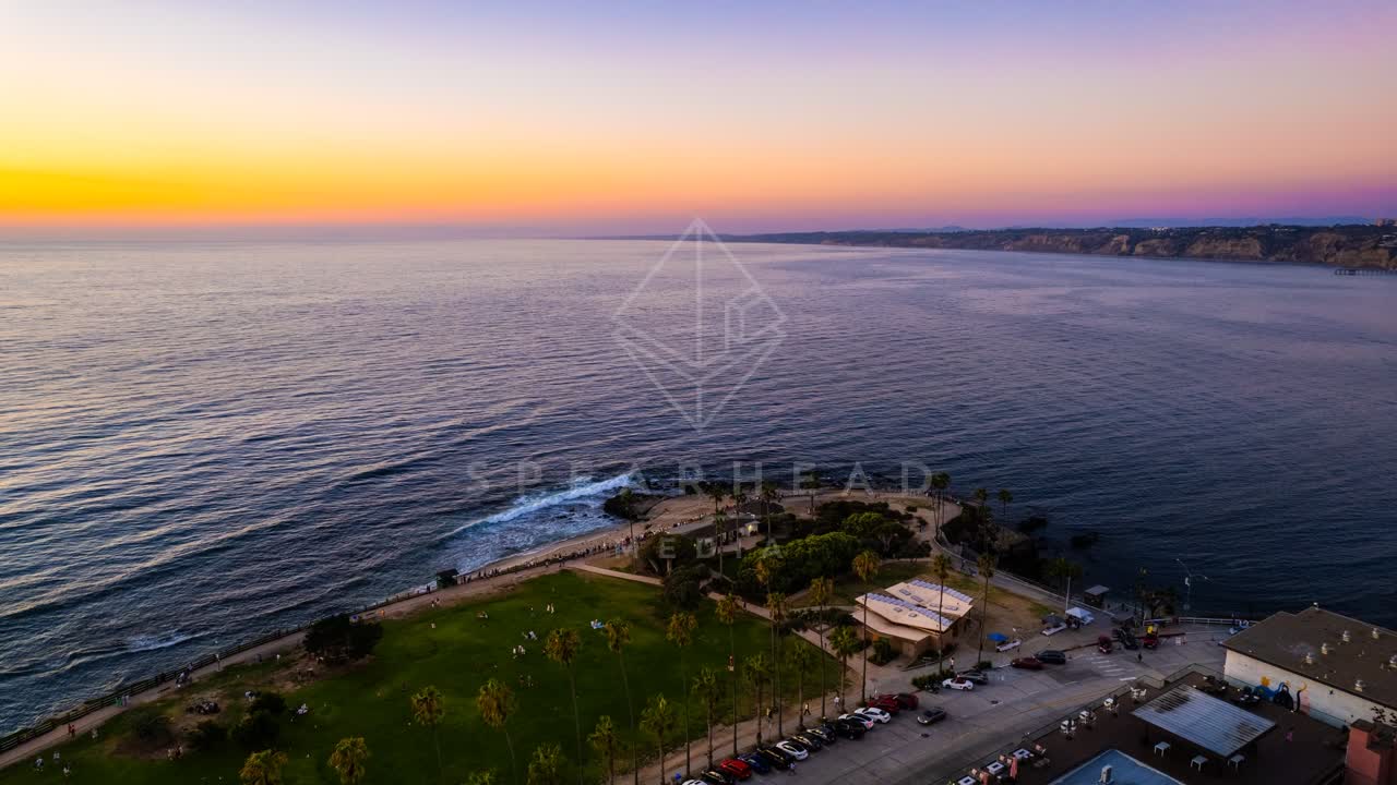 Aerial view of the cliffs, palm trees and the ocean at La Jolla Cove, with people walking.
