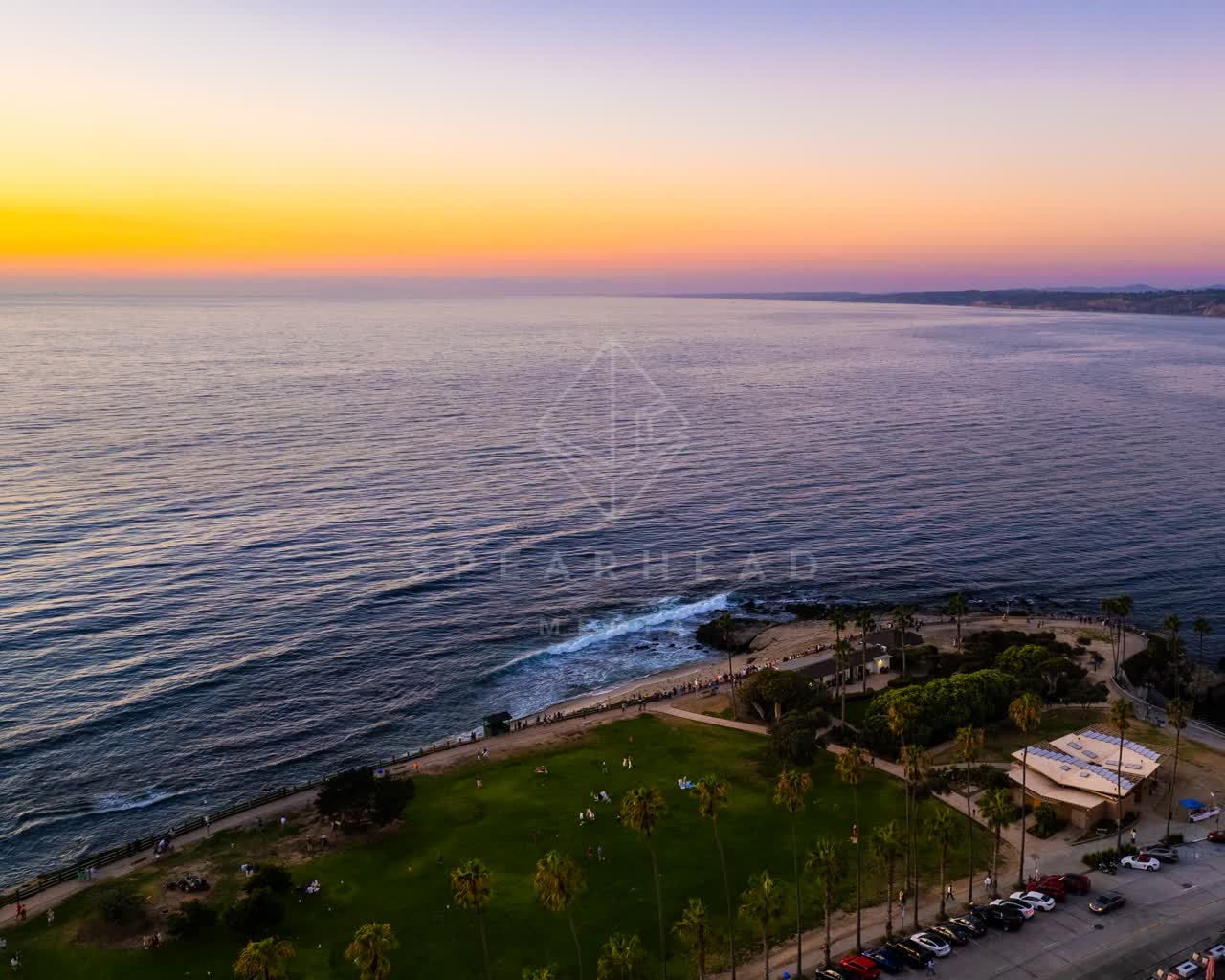 Aerial view of the cliffs, the surf and palm trees at La Jolla Cove, with people walking.