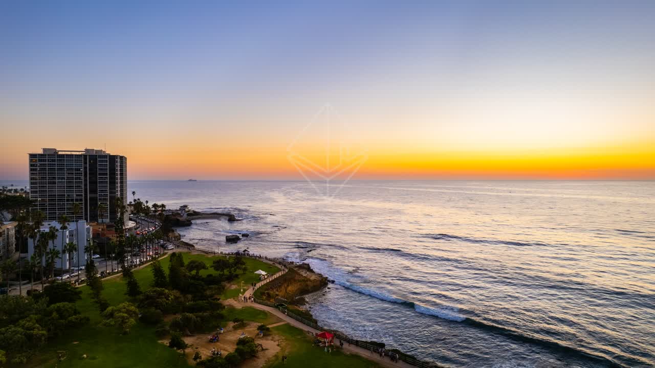 Aerial view of the cliffs, palm trees and the ocean at La Jolla Cove, with people walking.