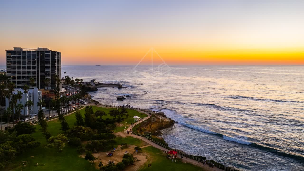 Aerial view of the cliffs, the surf and palm trees at La Jolla Cove, with people walking.
