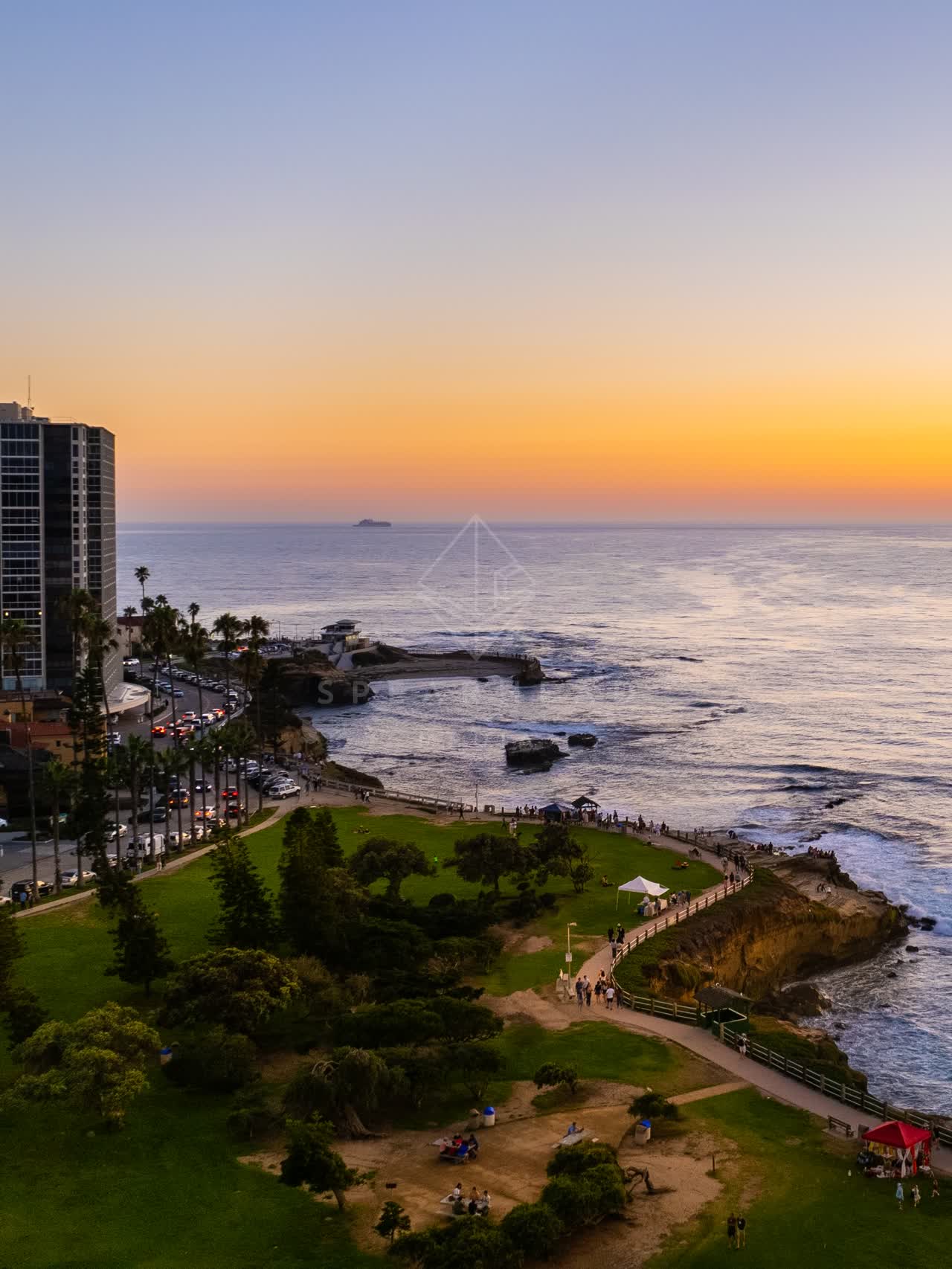 Aerial view of the cliffs, palm trees and the ocean at La Jolla Cove, with people walking.