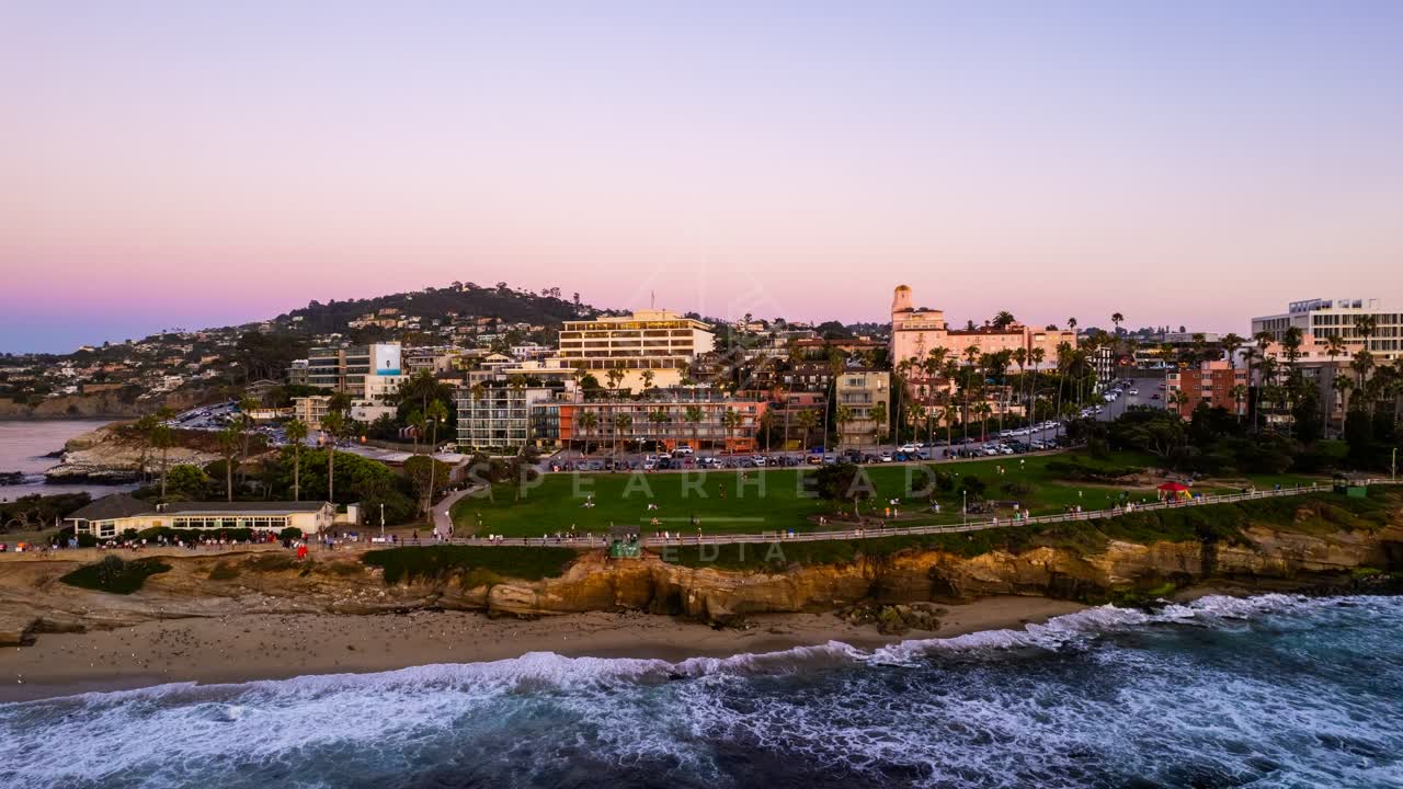 Aerial view of the cliffs, palm trees and the ocean at La Jolla Cove, with people walking.