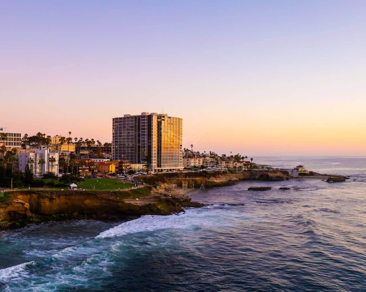 Aerial view of the cliffs, palm trees and the ocean at La Jolla Cove, with people walking.
