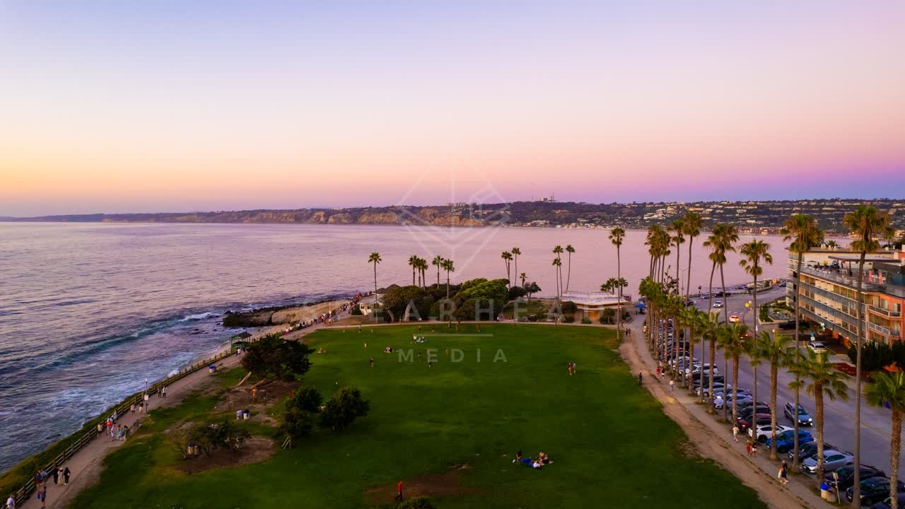 Low aerial view of a park, palm trees and the ocean at La Jolla Cove, with people walking.