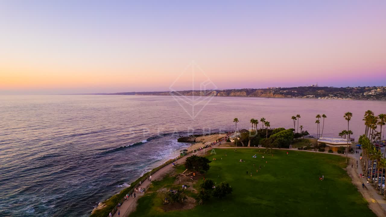 Aerial view of the beach, palm trees and the ocean at La Jolla Cove, with a crowd gathered.