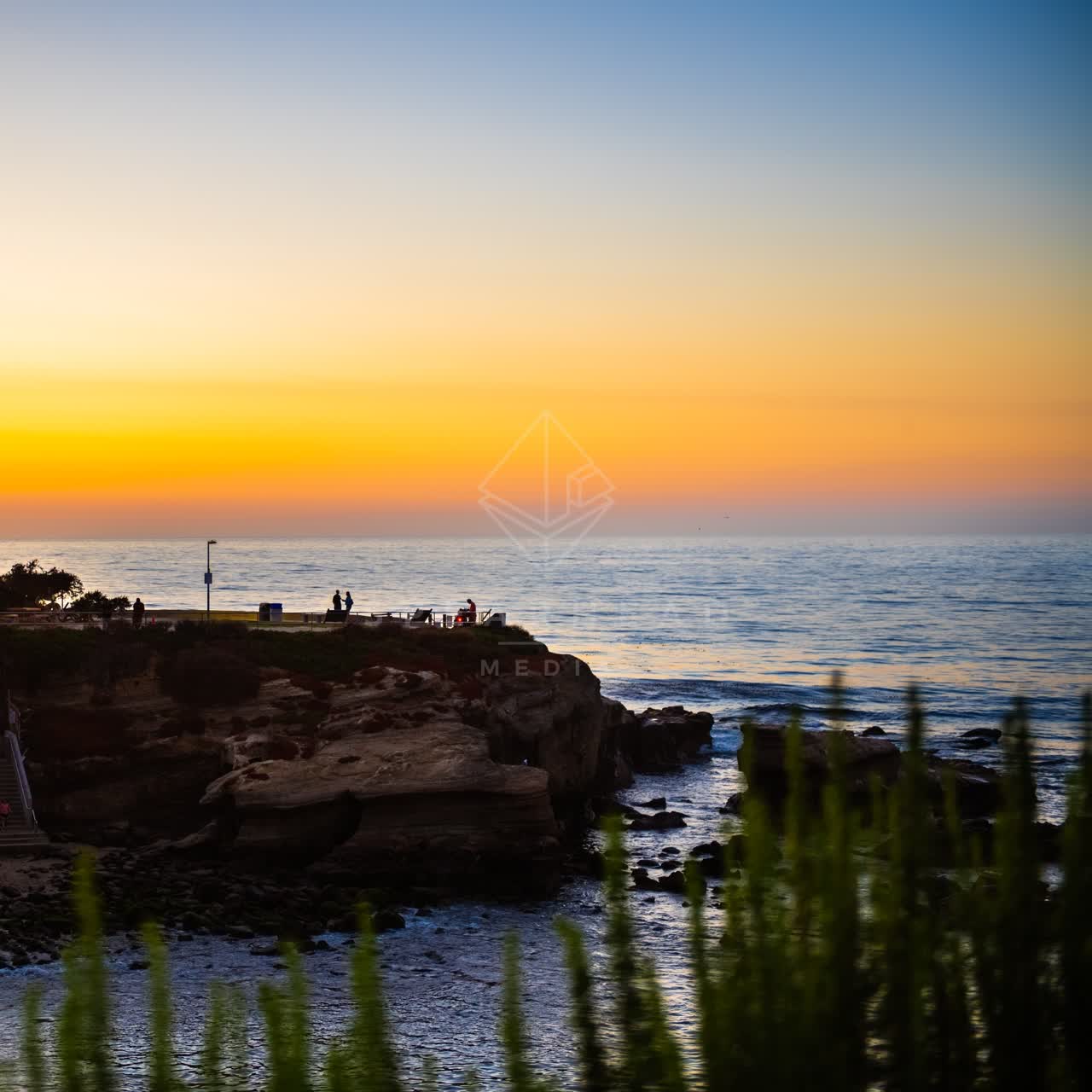 Elevated view of the cliffs, the ocean and open country at La Jolla Cove, with people walking.