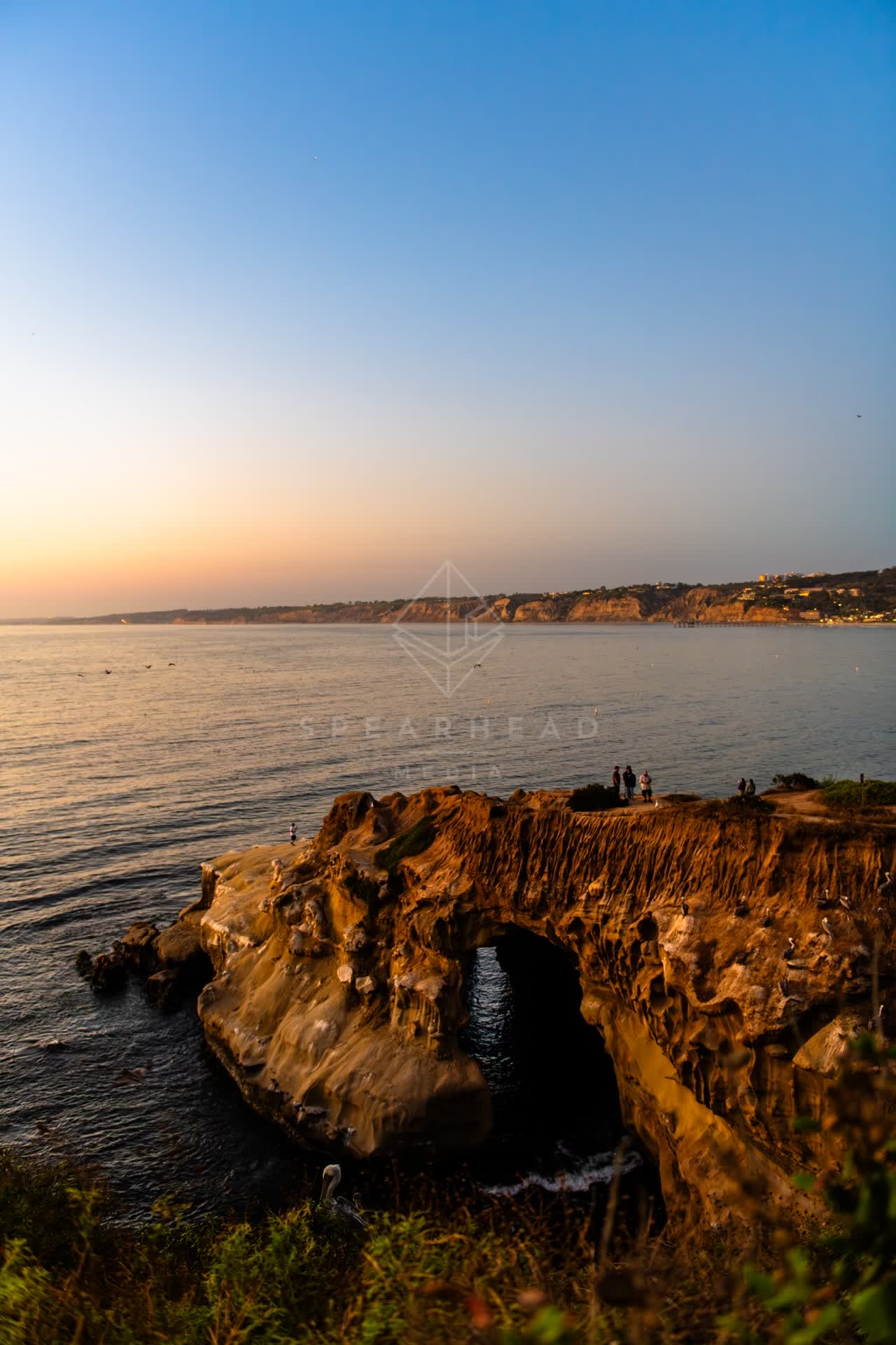 Elevated view of the cliffs, the ocean and open country at La Jolla Cove, with people walking.