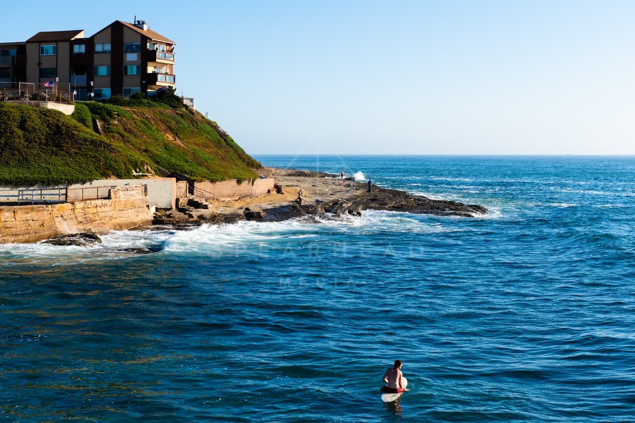 Elevated view of the cliffs, the surf and the ocean in Ocean Beach, with paddlers on the water.