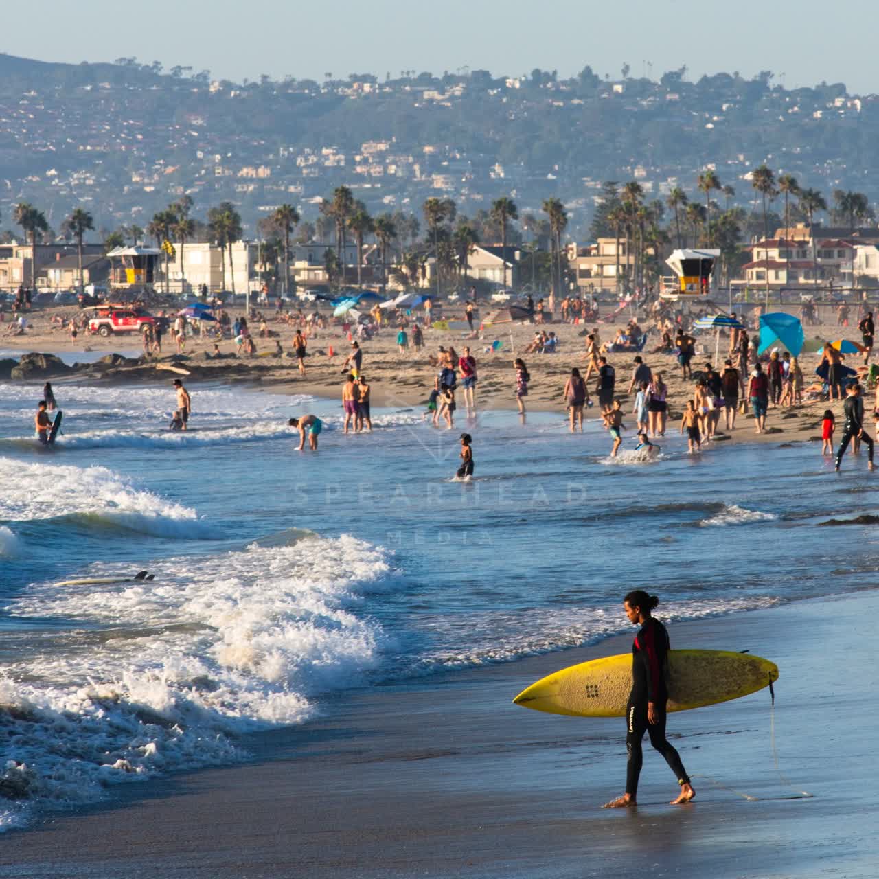 Elevated view of the beach, the surf and palm trees in Ocean Beach, with people walking.