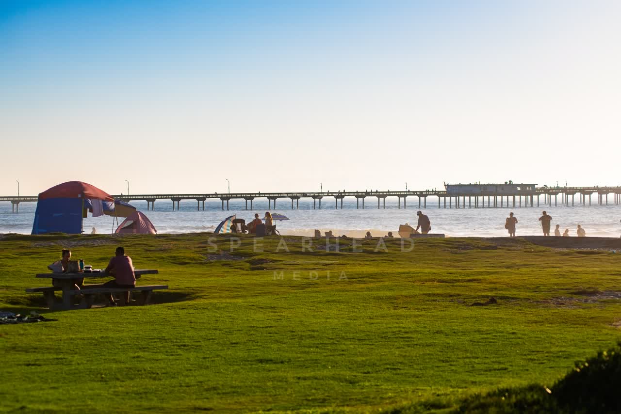 The beach, the pier and the ocean in Ocean Beach, with a crowd gathered.