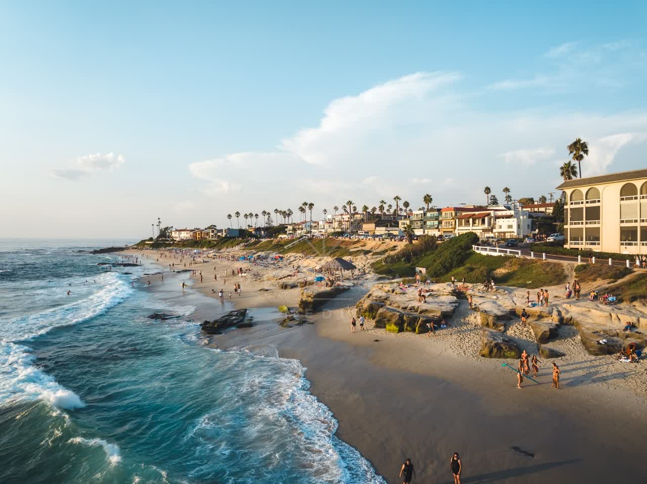Low aerial view of the beach, the surf and palm trees at Windansea, with people walking.