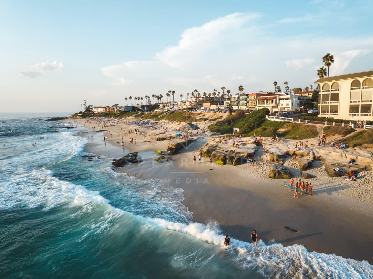 Low aerial view of the beach, the surf and palm trees at Windansea, with people walking.
