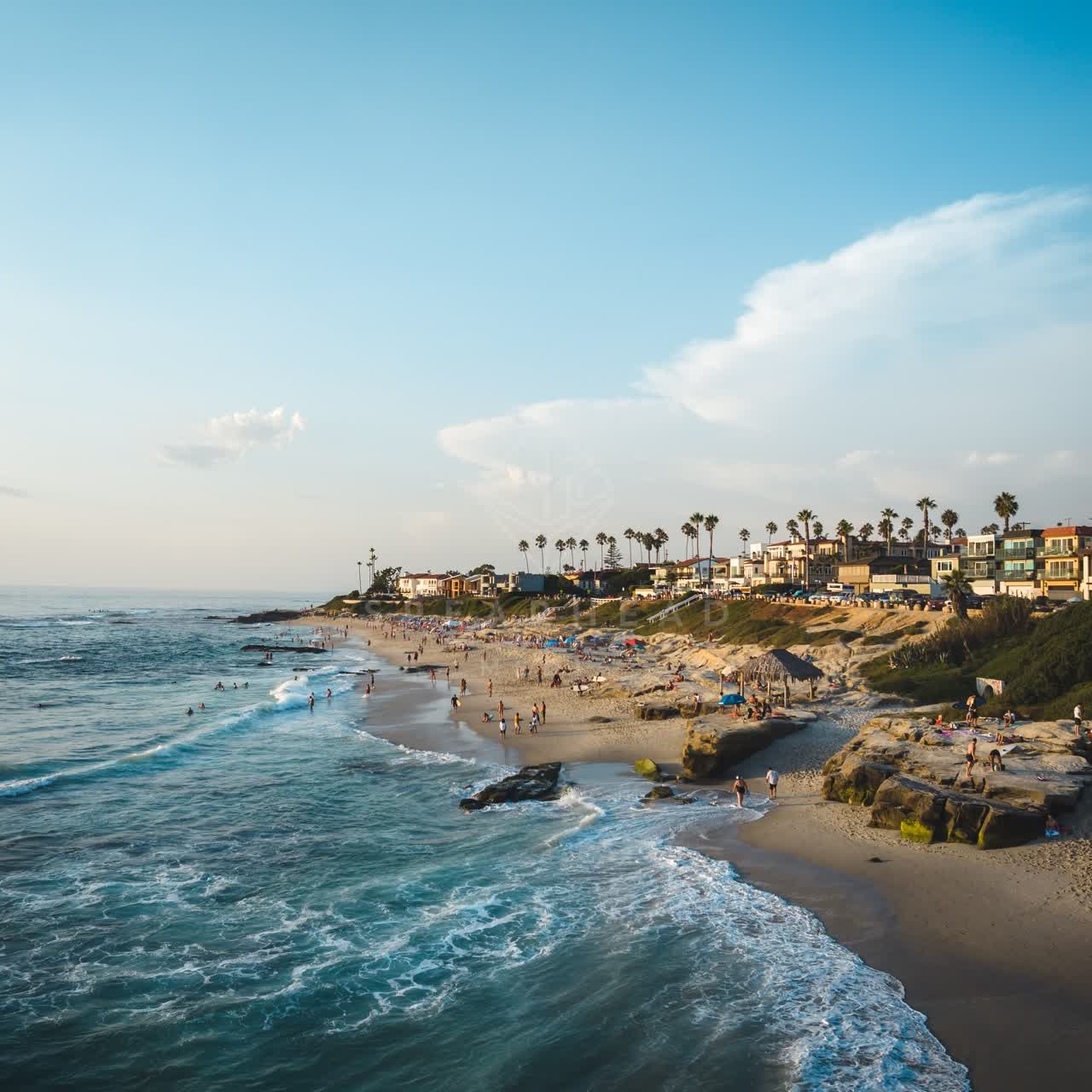 Low aerial view of the beach, the surf and palm trees at Windansea, with people walking.