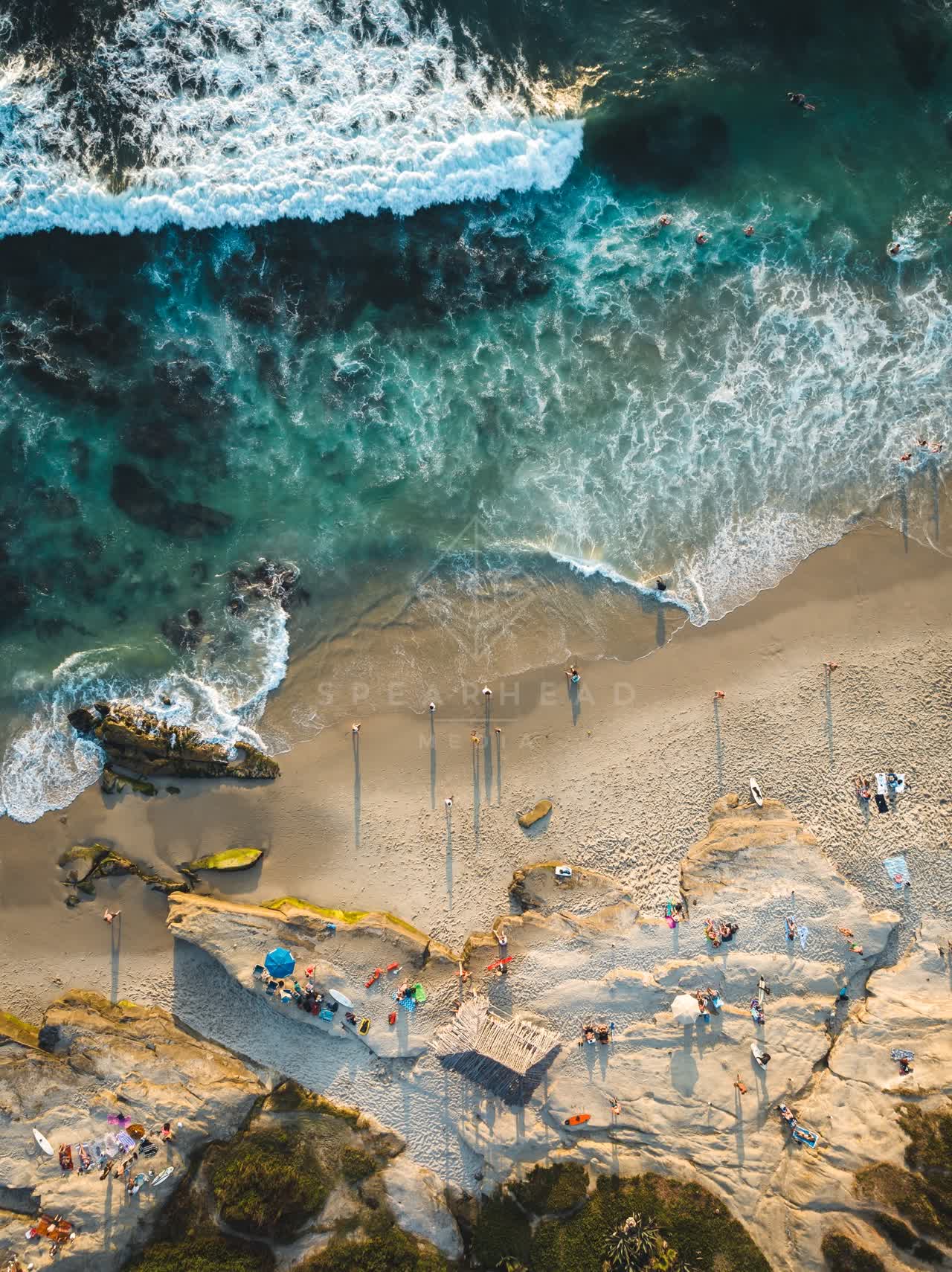 Aerial view of the beach, the surf and boats at Windansea, with a crowd gathered.
