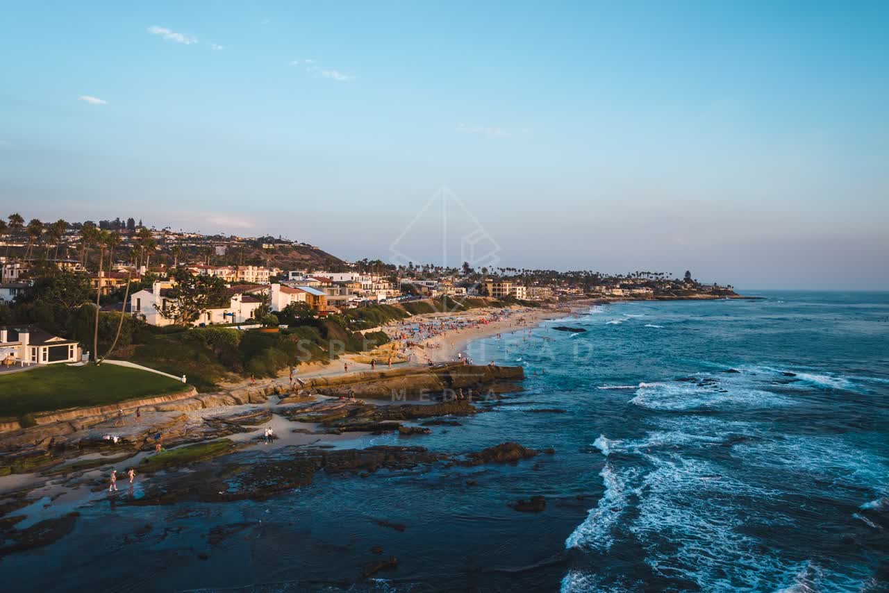 Aerial view of the beach, the surf and palm trees at Windansea, with a crowd gathered.