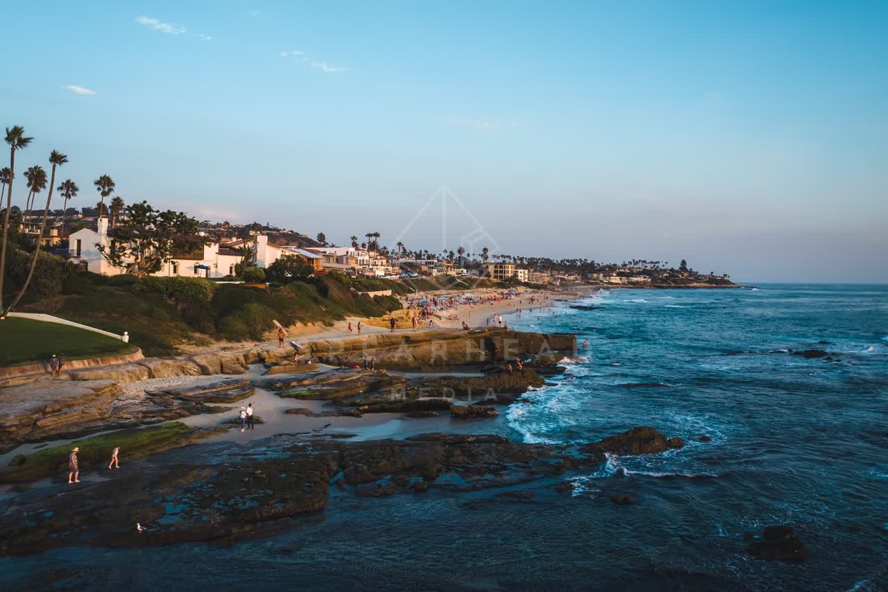 Low aerial view of the cliffs, palm trees and the ocean at Windansea, with people walking.