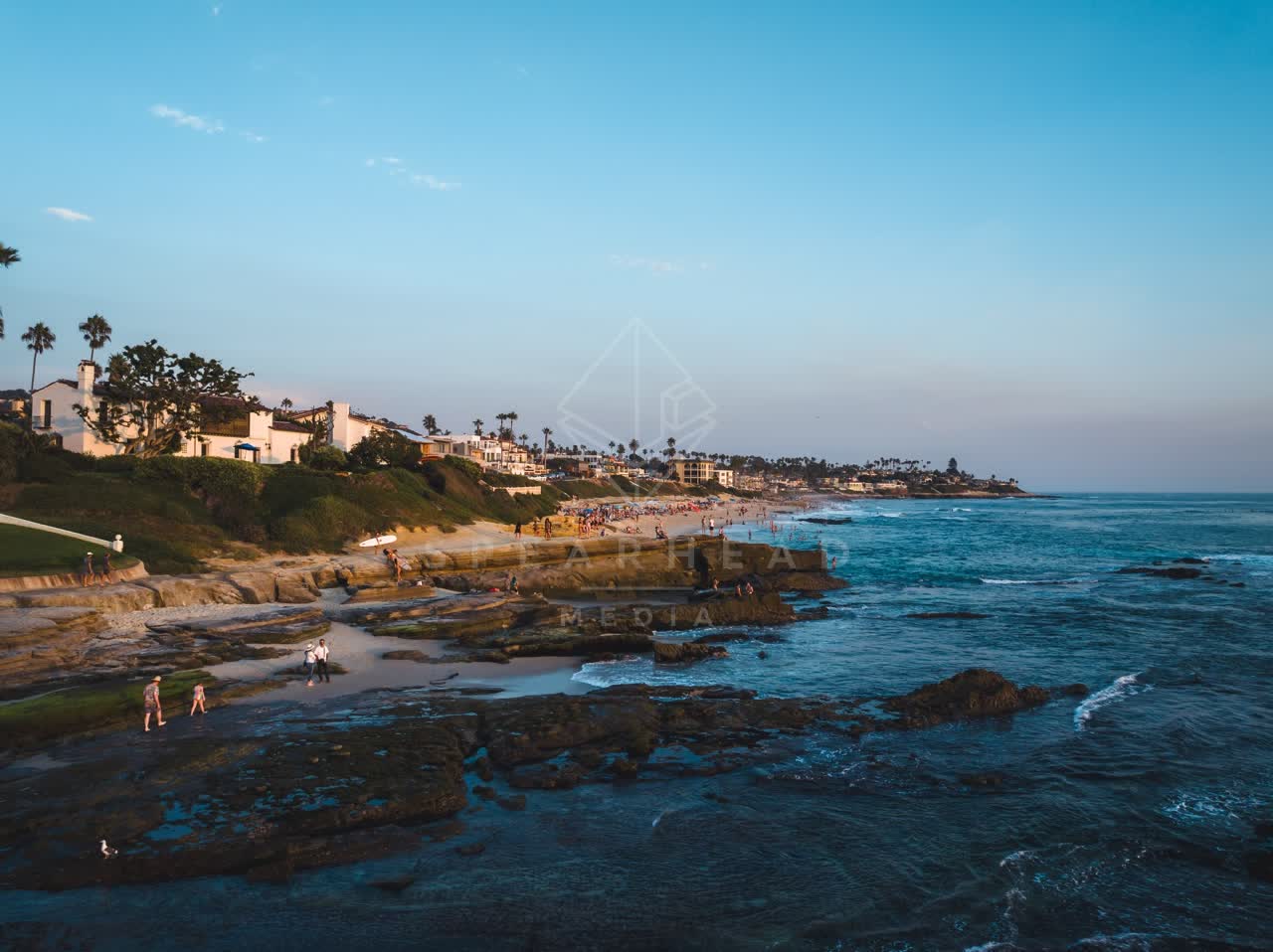 Low aerial view of the cliffs, palm trees and the ocean at Windansea, with people walking.
