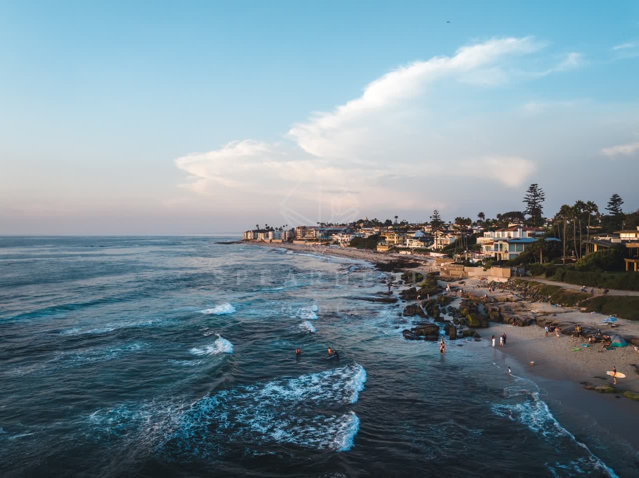 Aerial view of the beach, the surf and palm trees at Windansea, with people walking.