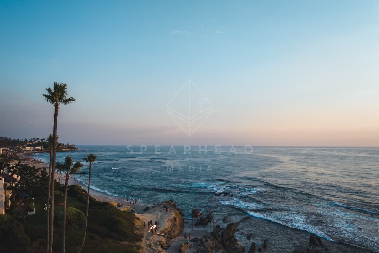 The cliffs, the surf and palm trees at Windansea, with people walking.