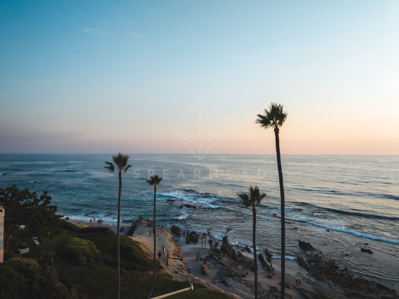 Low aerial view of the cliffs, palm trees and the ocean at Windansea, with people walking.