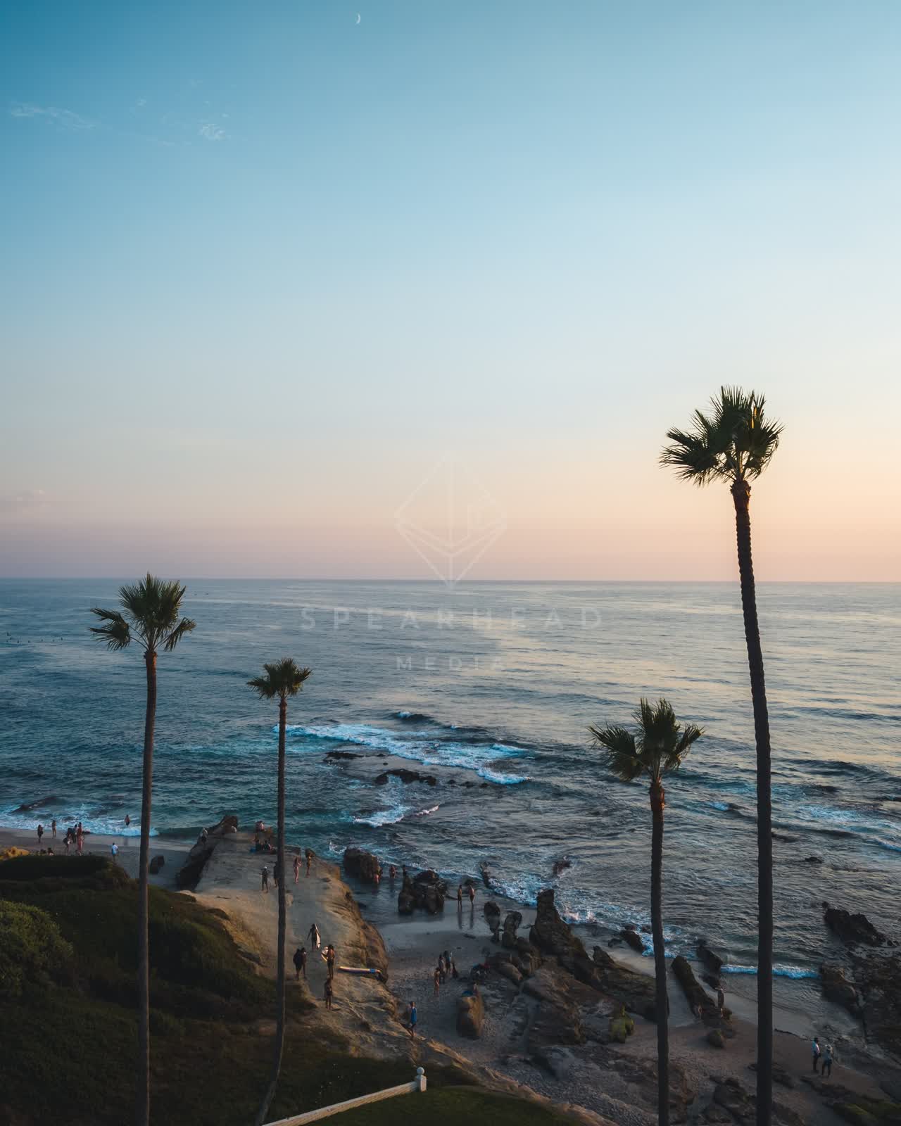Elevated view of the cliffs, palm trees and the ocean at Windansea, with people walking.