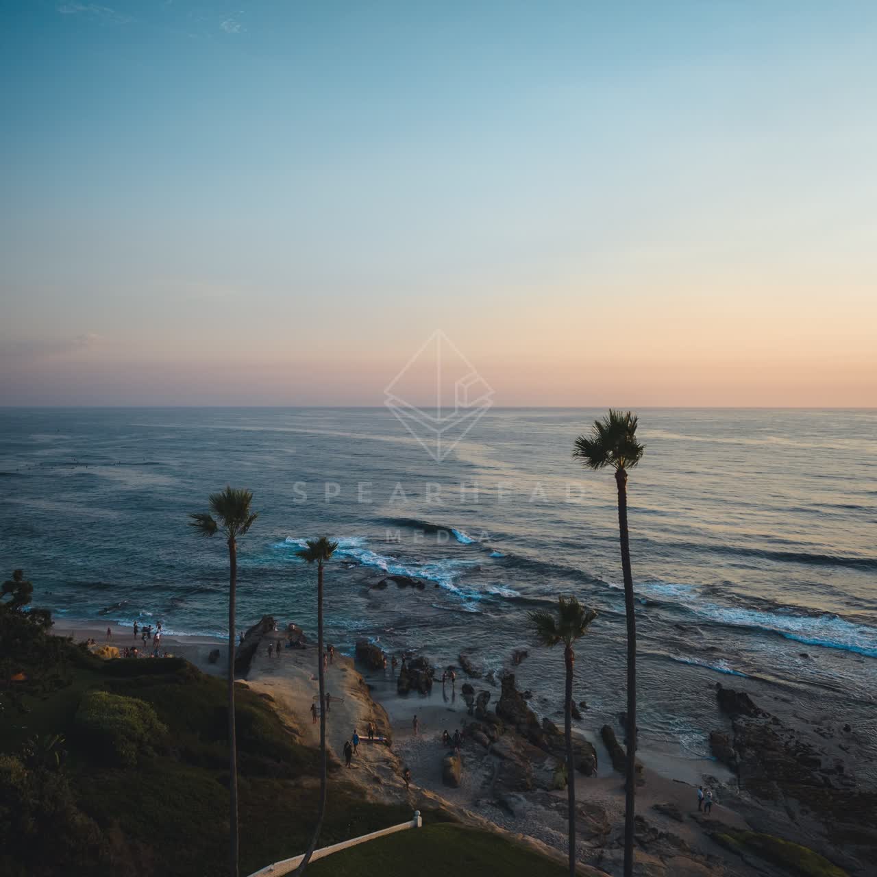Elevated view of the cliffs, the surf and palm trees at Windansea, with a crowd gathered.