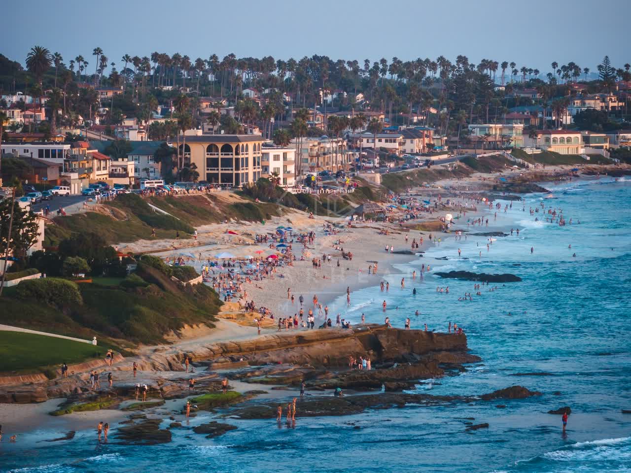 Aerial view of the beach, palm trees and the ocean at Windansea, with a crowd gathered.
