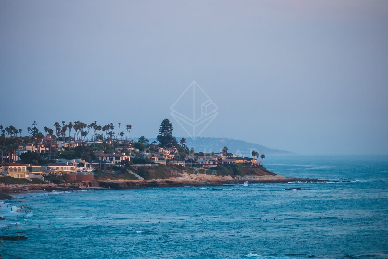 Low aerial view of the cliffs, palm trees and the ocean at Windansea, with swimmers in the water.